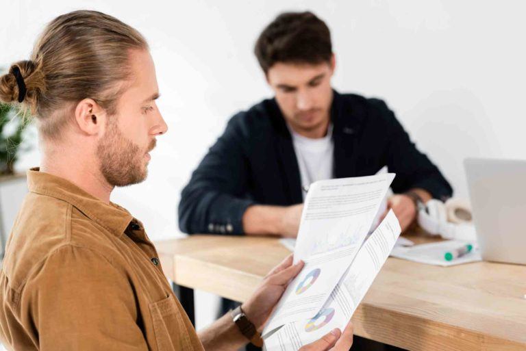 Mann sitzt neben einem Tisch und hält Vertrag in der Hand